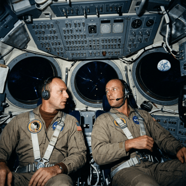 Two Apollo 11 astronauts seated inside the lunar module with Earth visible through window
